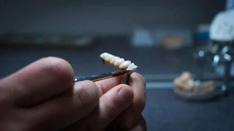 A dental technician using a fine brush to carefully apply detail and finish a set of realistic zirconia crowns in a laboratory.